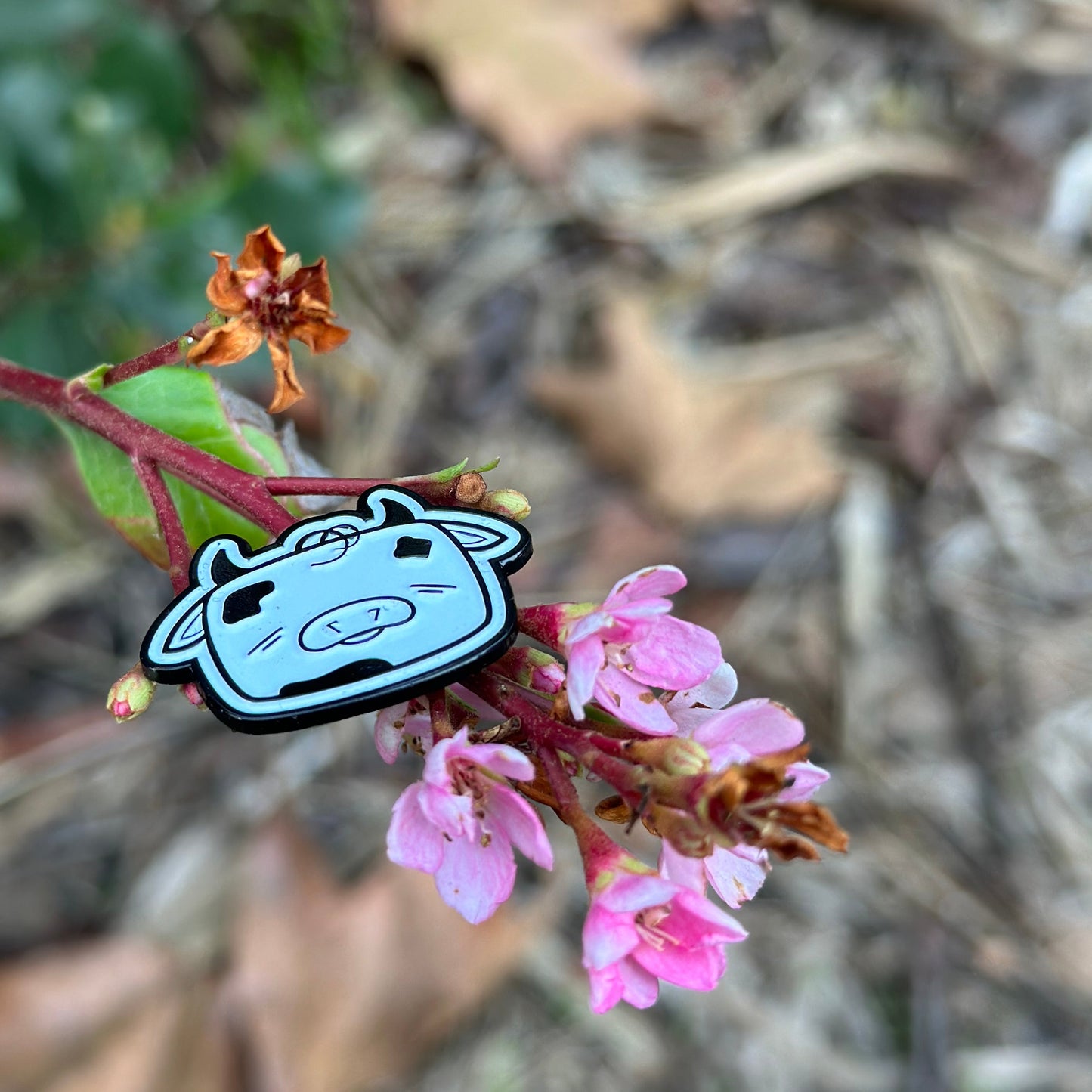 Small cartoon character attached to a pink flower with a blurred natural background